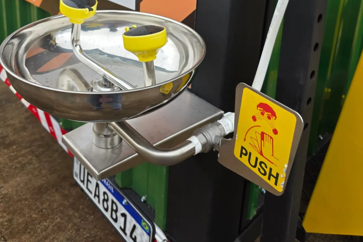 Detalhe do lava-olhos em aço inox com dois jatos amarelos e botão de acionamento PUSH