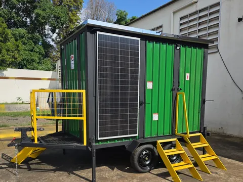Unidade verde longa com placas solares e escadas amarelas, sob luz dourada no pátio