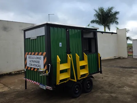 Unidade verde compacta com placa de segurança e rampa amarela, vista de frente no pátio