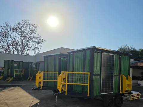Pátio ao pôr do sol com unidades verdes alinhadas e sol brilhando entre as árvores