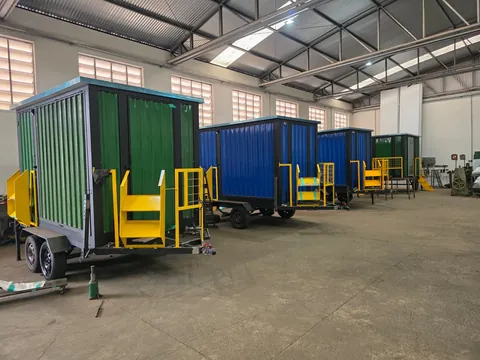 Galpão de fabricação com unidades verdes e azuis em produção, estrutura metálica ao fundo