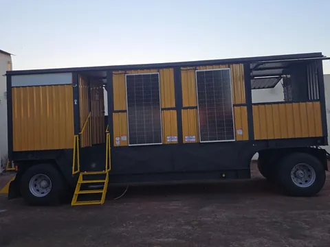 Trailer amarelo com escadas de acesso e módulo de janelas, visto de lado no pátio
