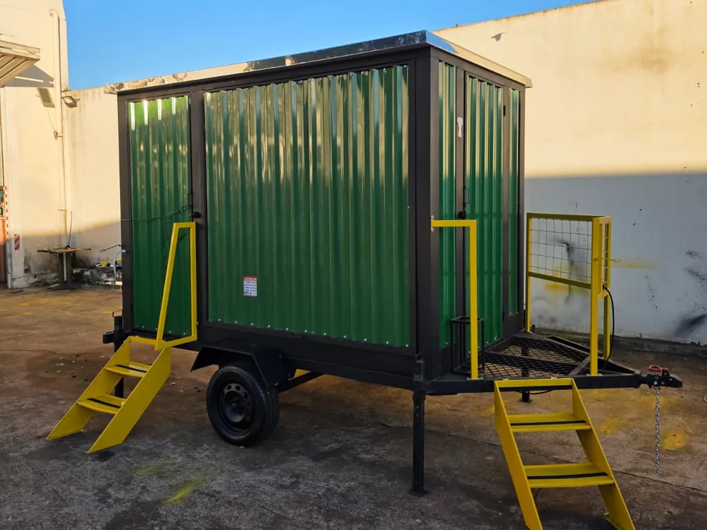 Unidade compacta verde com duas escadas amarelas e plataforma lateral, no pátio da fábrica