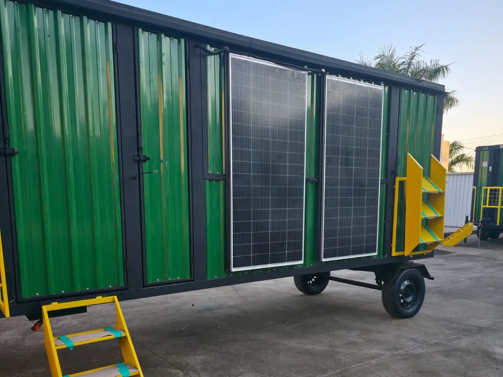 Unidade longa verde com painéis solares na lateral, escada amarela e pátio cimentado ao redor